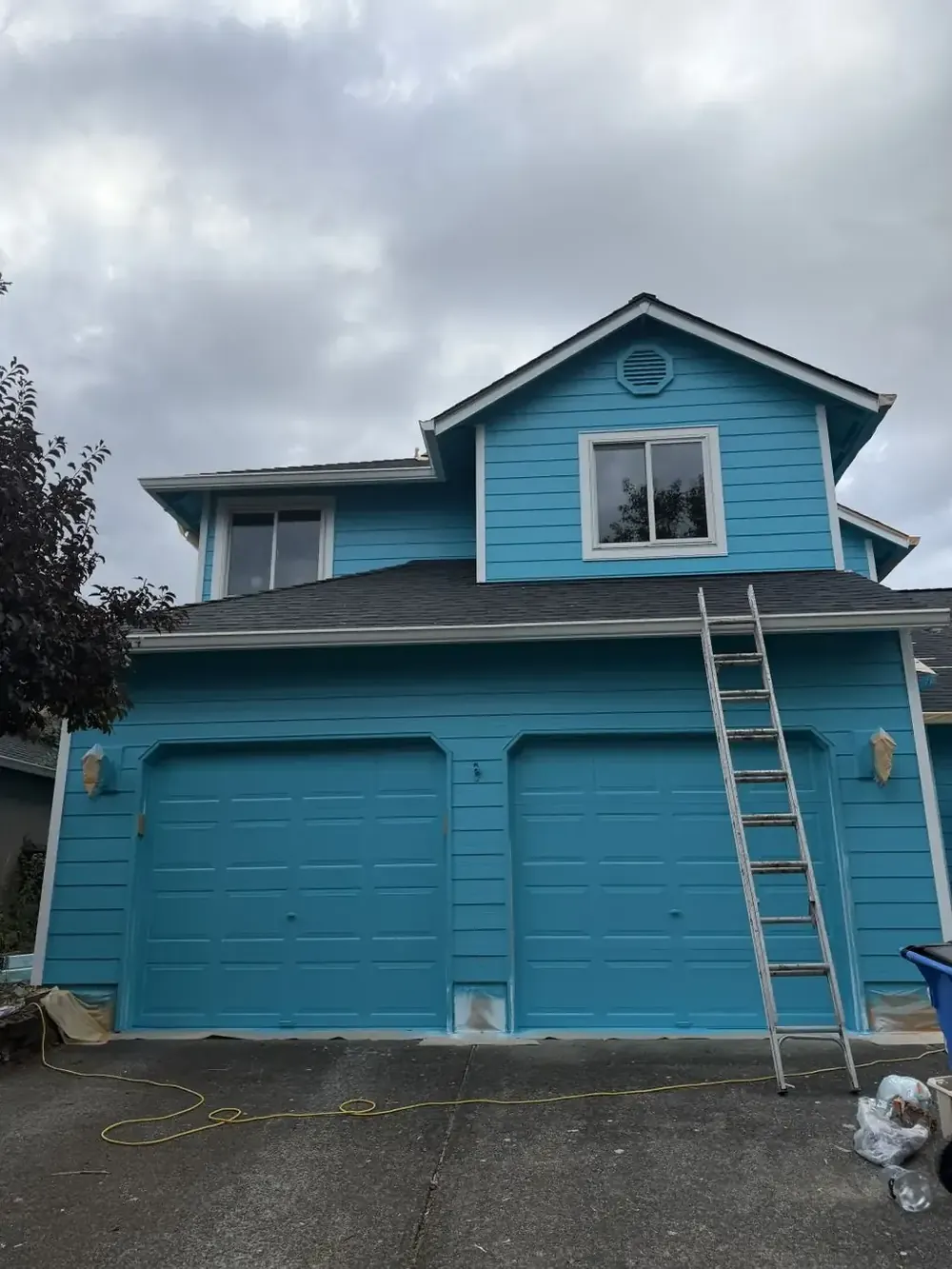 Blue two-story house with a ladder during exterior painting