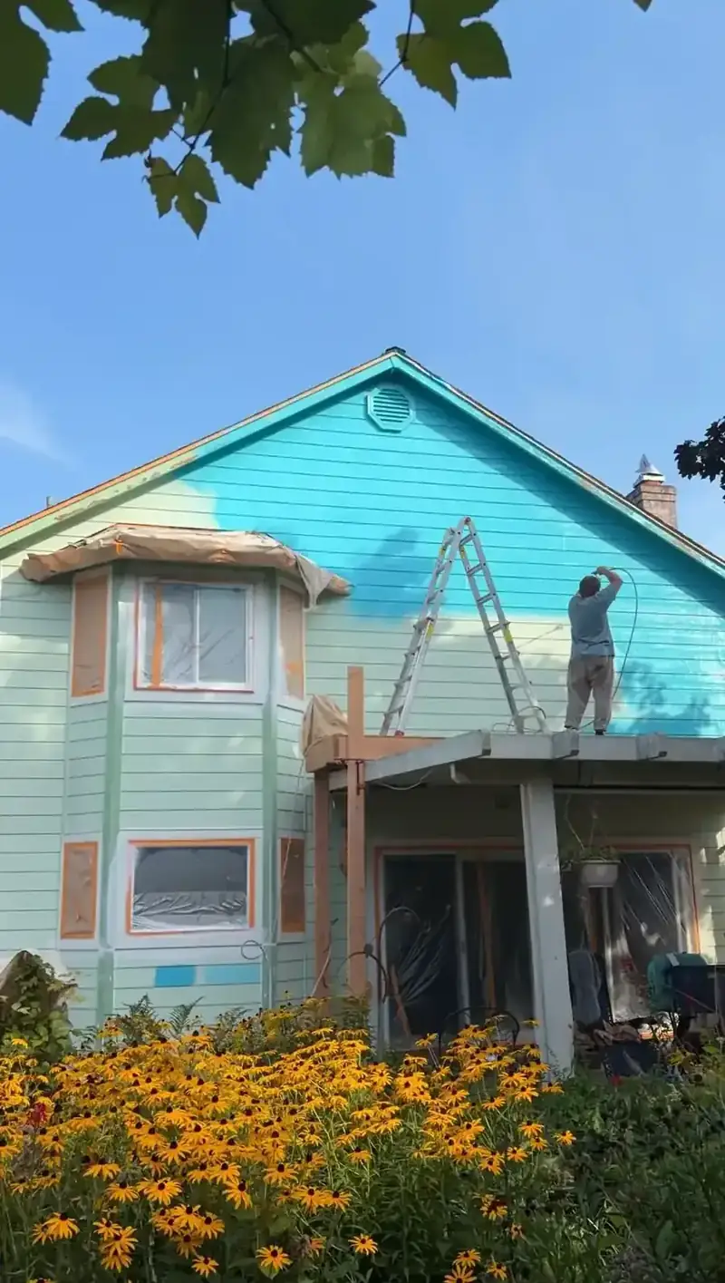 House exterior painting in progress with a painter on a ladder